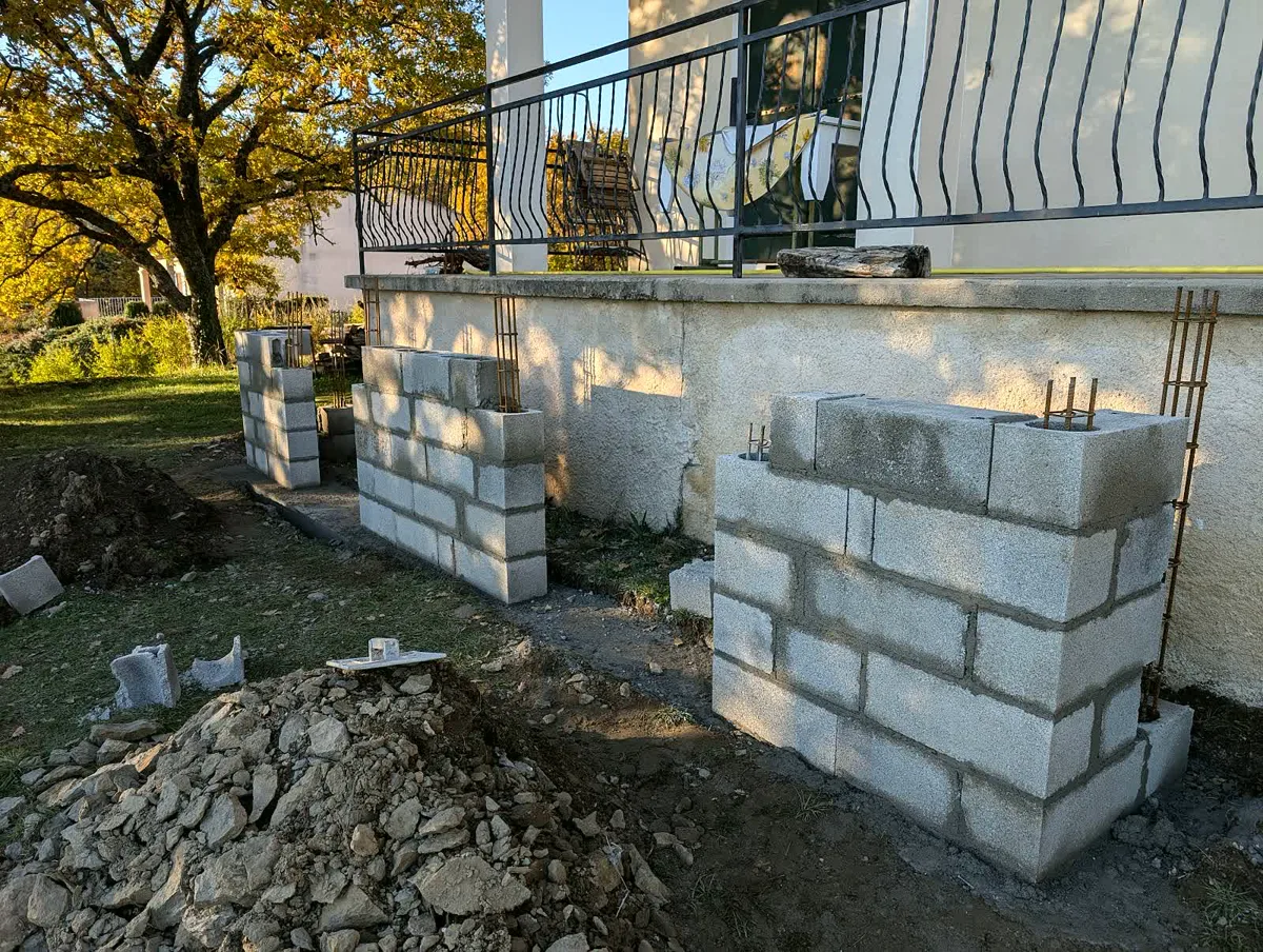 Piliers en parpaing ferraillés en cours de montage le long d'un mur